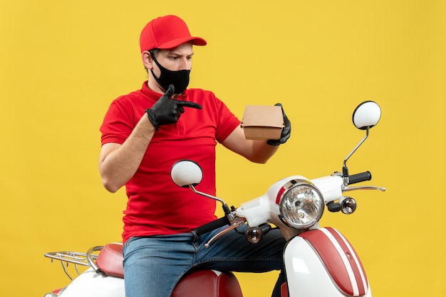 Free photo top view of surprised confused delivery guy wearing red blouse and hat gloves in medical mask sitting on scooter showing order