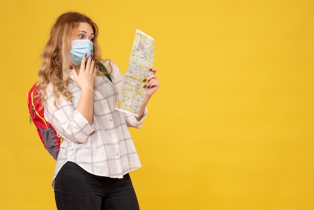 Free photo top view of surprised travelling girl wearing her mask and backpack looking at map on yellow