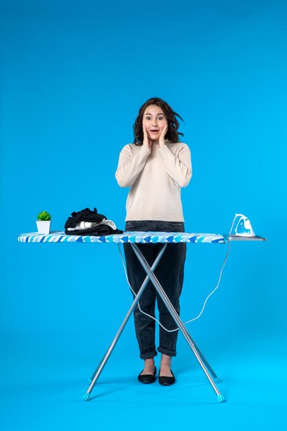 Top view of surprised young girl standing behind the ironing board on blue wave surface