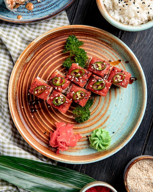 top view of sushi rolls with tuna on a plate with ginger and wasabi on wooden surface