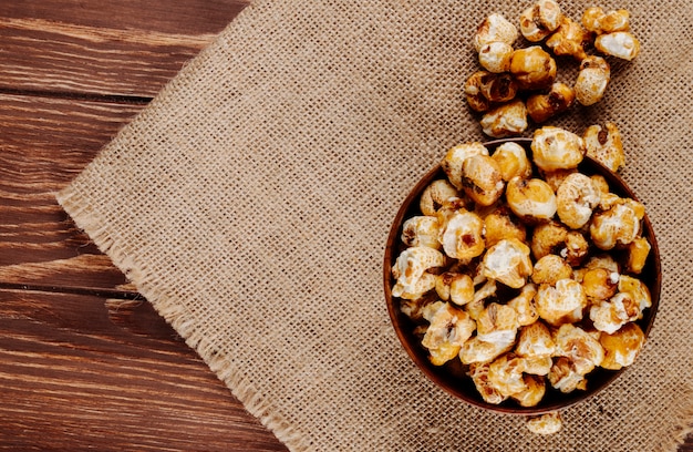 Top view of sweet caramel popcorn in a wooden bowl on sackcloth on rustic background with copy space