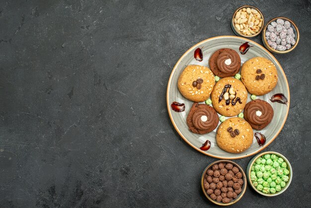 Top view sweet cookies with candies on dark-grey background sugar cookie sweet biscuit cake tea