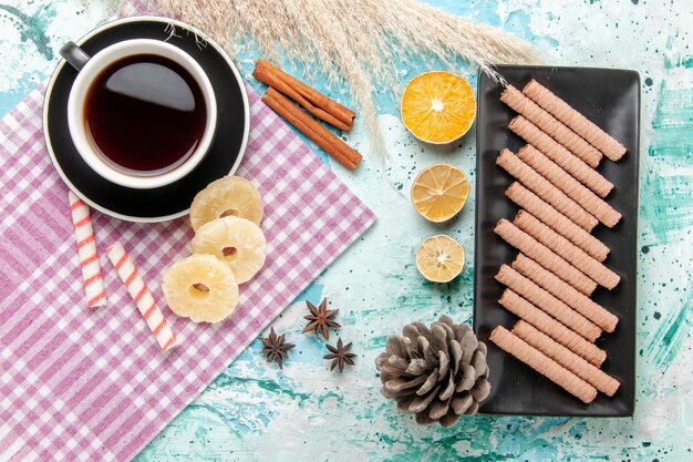 Top view sweet cookies with cup of tea and dried pineapple rings on blue background