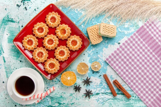 Top view sweet cookies with orange jam and cup of tea on light-blue background