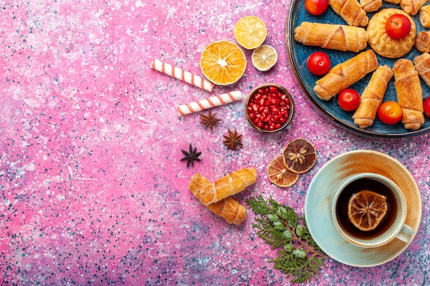 Free Photo top view sweet delicious bagels inside tray with plums and cup of tea on pink surface