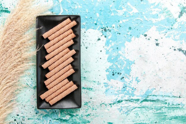 Top view sweet long cookies inside black cake pan on blue background