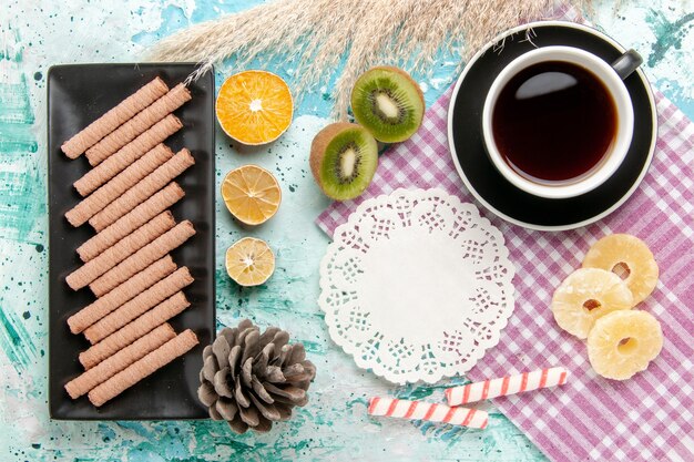 Top view sweet long cookies with cup of tea and dried pineapple rings on the blue desk