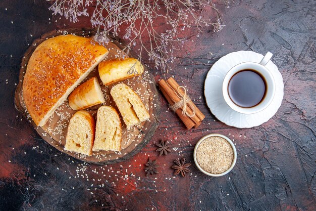 Top view sweet pastry sliced in pieces with cup of tea on dark surface