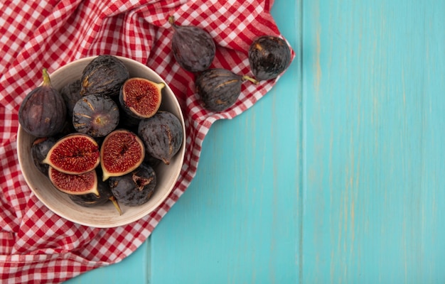 Free photo top view of sweet ripe black mission figs on a bowl on a checked cloth on a blue wooden wall with copy space