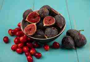 Free photo top view of sweet ripe black mission figs on a bowl with cornelian cherries isolated on a blue wooden wall