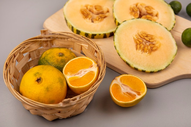 Top view of sweet slices of cantaloupe melon with feijoas isolated on a wooden kitchen board with tangerines on a bucket on a grey wall