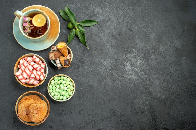 Top view of sweets a cup of tea cookies colorful sweets citrus fruits with leaves