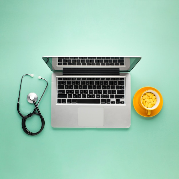 Free Photo top view of tablets on cup with laptop and stethoscope over green desk