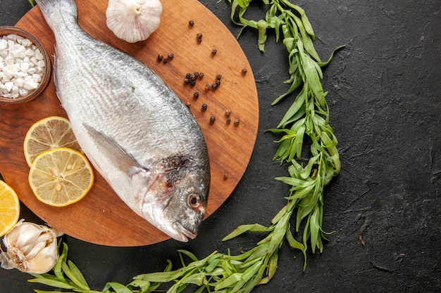 Top view tarragon circle around fresh raw fish garlic sea salt in bowl on round wood board on black