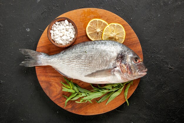 Top view tarragon raw sea fish sea salt in bowl lemon slices on round wood board on black