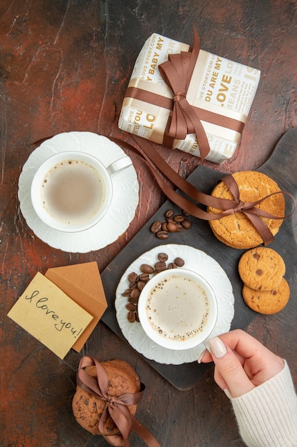 Top view tasty biscuits with cups of coffee and present on dark background cookie sweet tea couple love color cake morning