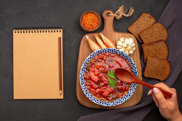 Top view tasty borsch ukranian beet soup with dark bread loafs on the dark space