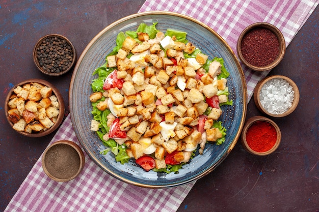 Top view tasty caesar salad with little rusks and seasonings on the dark desk