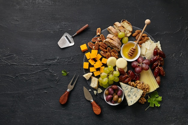 Free Photo top view of tasty cheese plate with fruit, grape, nuts and honey on a circle kitchen plate on the black stone background, top view, copy space. gourmet food and drink.