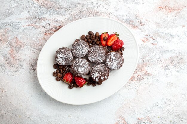 Top view tasty chocolate cakes with strawberries and chocolate chips on white surface