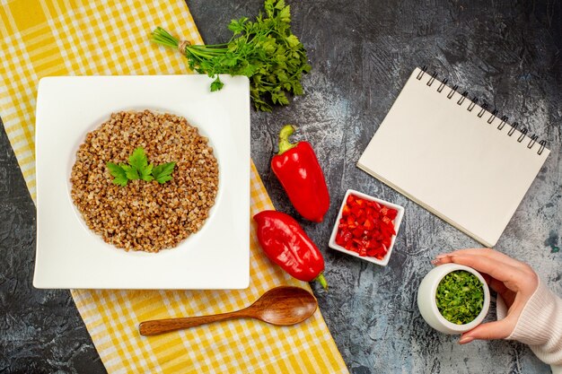 Top view tasty cooked buckwheat with greens and bell-peppers on light-grey table