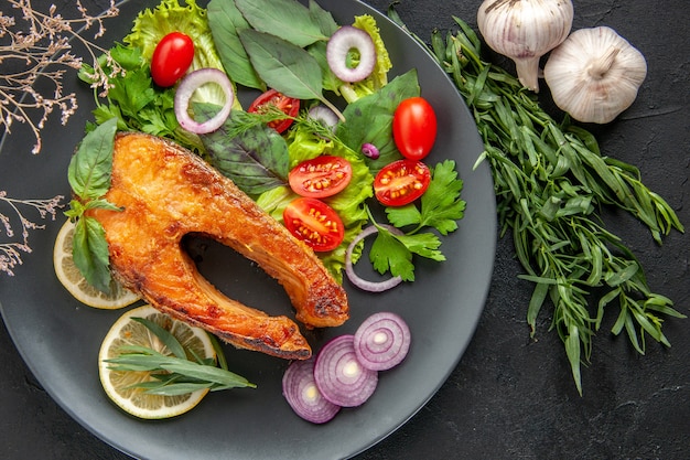 Top view tasty cooked fish with fresh vegetables and seasonings on dark table