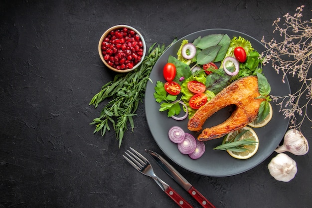 Top view tasty cooked fish with fresh vegetables and seasonings on the dark table