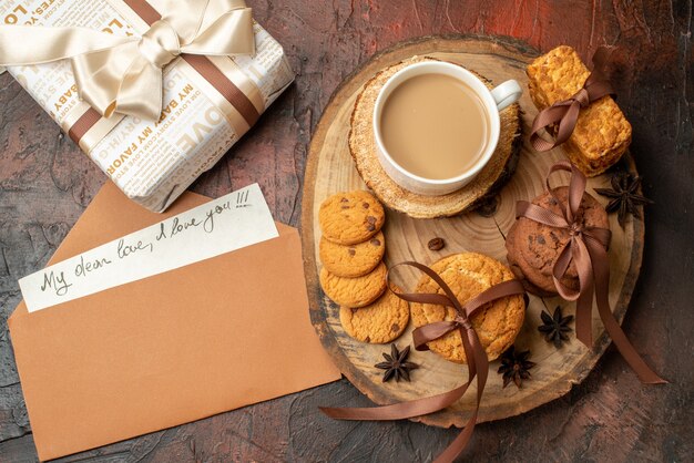 Top view tasty cookies tied with rope cup of coffee on wood board love letter in envelope gift on table