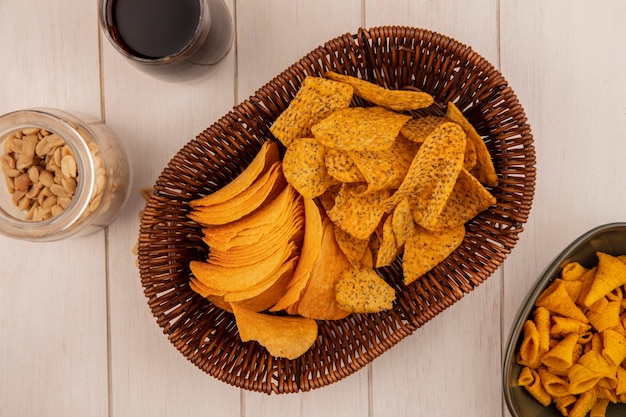 Top view of tasty crispy chips on a bucket with a glass of cola with pine nuts on a glass jar on a beige wooden table