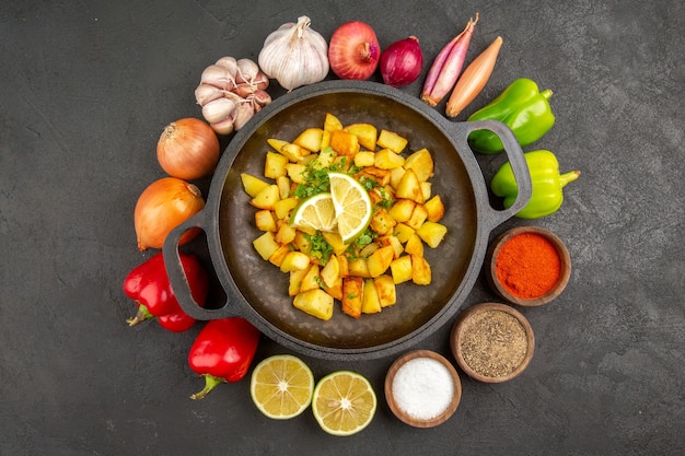 Free Photo top view of tasty fried potatoes inside pan with different seasonings and vegetables on dark surface