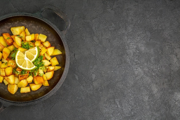 Free photo top view of tasty fried potatoes inside pan with lemon slices on dark surface