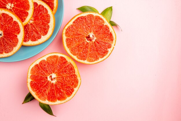 Top view of tasty grapefruits fruit slices inside plate on the pink surface