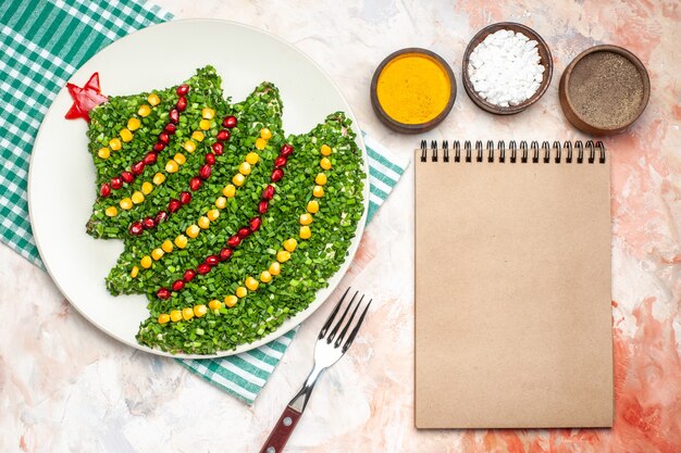 Top view tasty green salad in new year tree shape with seasonings on the light background