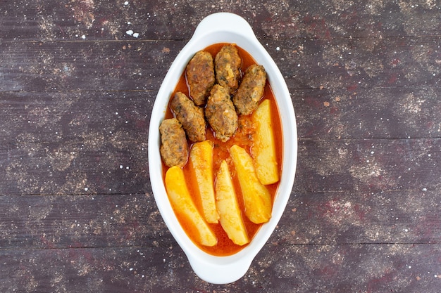 Top view tasty meat cutlets cooked along with potatoes and sauce inside plate on the brown background meat potato dish meal dinner