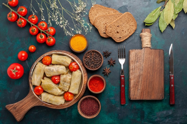 Top view tasty meat meal rolled inside cabbage with bread and fresh tomatoes on dark-blue desk