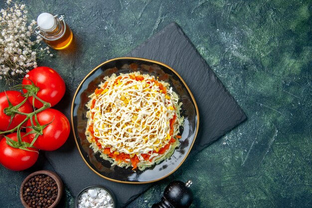 Top view of tasty mimosa salad inside plate with red tomatoes on dark blue surface