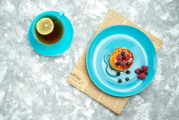 Top view of tasty muffins with berries and cup of tea on light surface