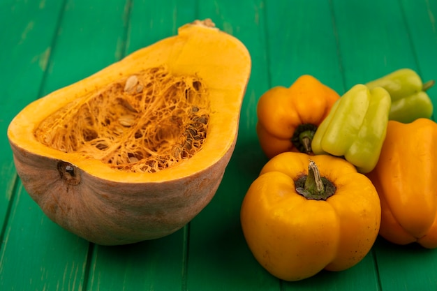 Free photo top view of tasty orange pumpkin with its seeds with bell peppers isolated on a green wooden wall