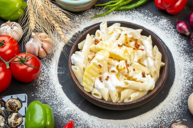 Top view tasty penne pasta in bowl red onions garlic quail eggs tomatoes on table