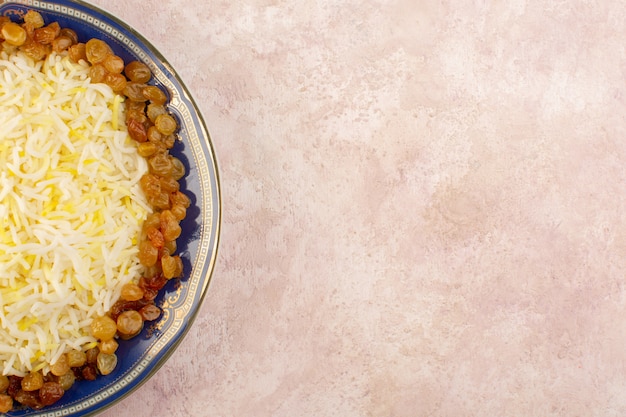 Free photo a top view tasty pilaf with oil and dried raisins inside plate on the pink surface