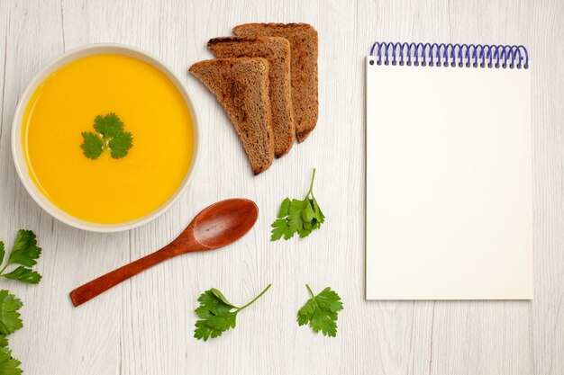 Top view of tasty pumpkin soup cream textured with dark bread loafs on light white