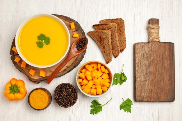 Top view of tasty pumpkin soup with dark bread loafs and seasonings on white