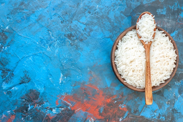 Free Photo top view of tasty rice meal in a brown small pot and wooden spoon on the left side on blue table