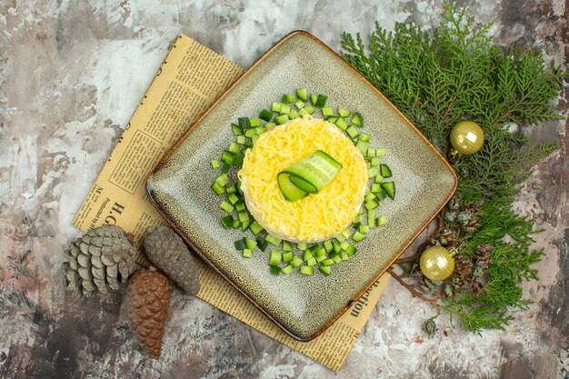 Top view of tasty salad served with chopped cucumber and knife fork on an old newspaper