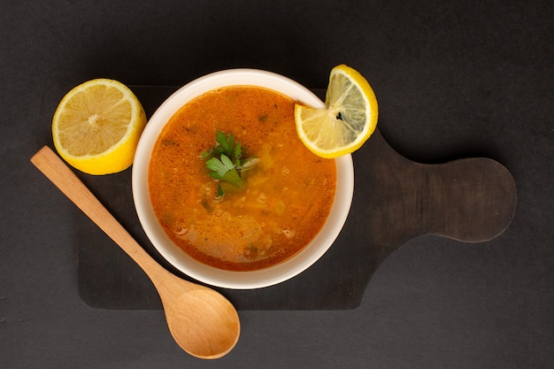 Top view of tasty vegetable soup inside plate along with lemon on dark surface