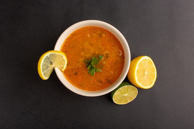 Top view of tasty vegetable soup inside plate along with lemon on dark surface