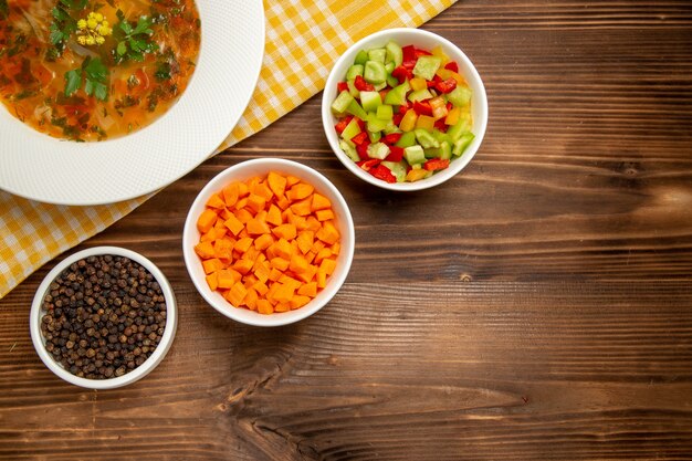 Top view tasty vegetable soup with sliced vegetables on brown wooden desk soup food vegetables seasonings