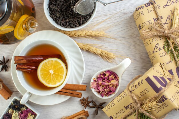 Top view of tea break with cinnamon lime and lemon in a cup and pot around necessary ingredients next to gifts on white background