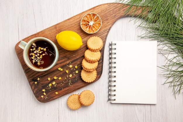 Top view tea and lemon a cup of tea with herbs cookies and lemon on the kitchen board white notebook and Christmas tree branches