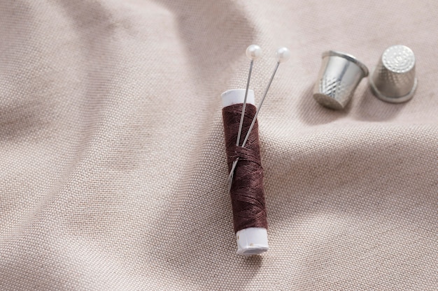 Top view of thread reel with needles and thimbles on textile